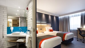 Ein Hotelzimmer mit Bad, zwei Betten, einem Schreibtisch und einem großen Fenster.