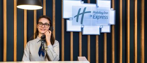 Un comptoir d’accueil d’hôtel au design moderne, avec un mur revêtu de panneaux en bois et une enseigne « Holiday Inn Express ».