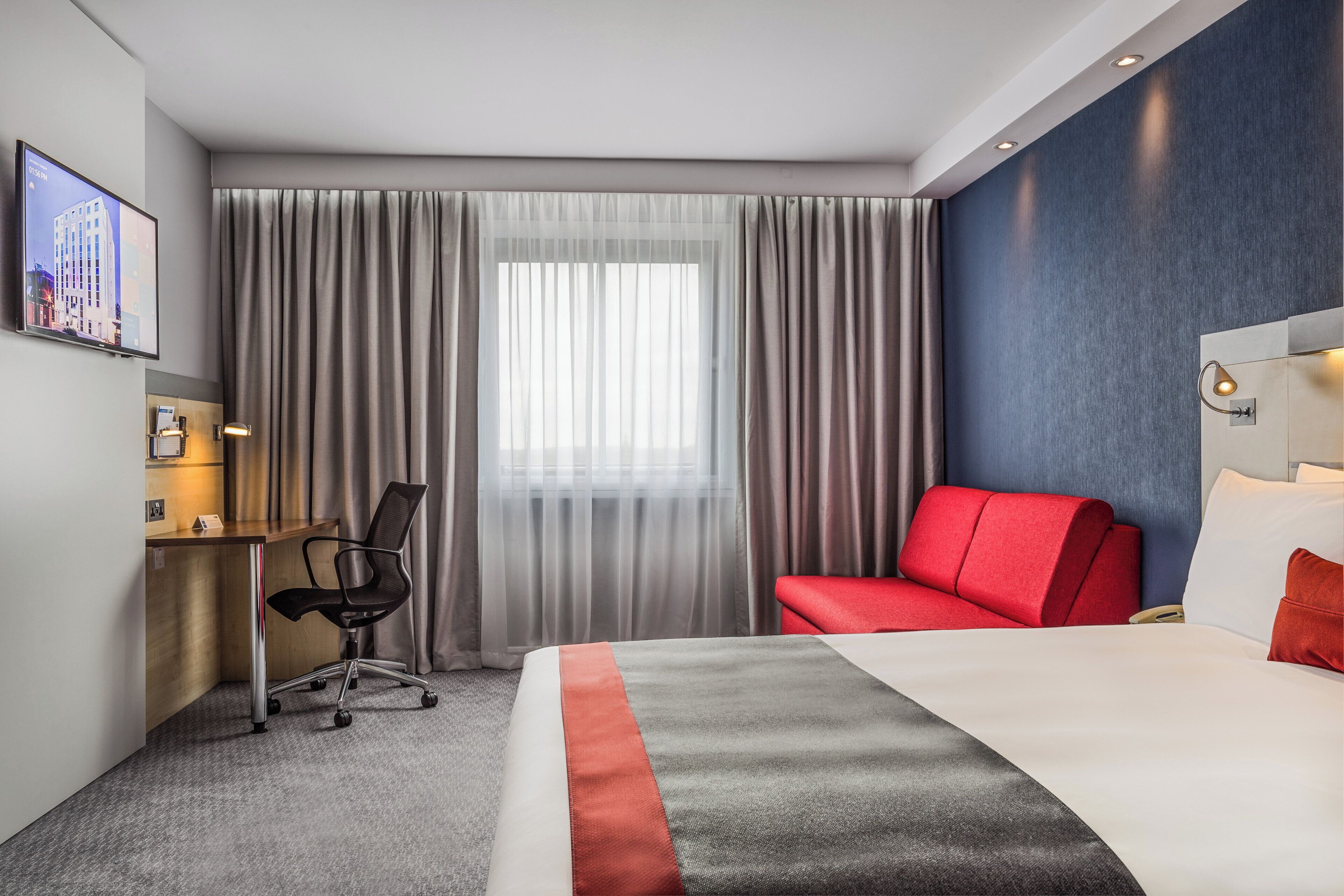 A hotel room with a bed, a desk, a chair, and a television.