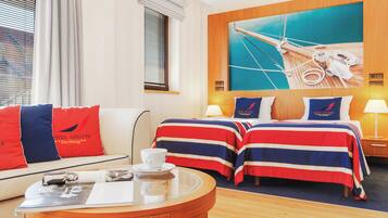 A hotel room with two beds, a sofa, a round table, and a large painting of a ship's deck.