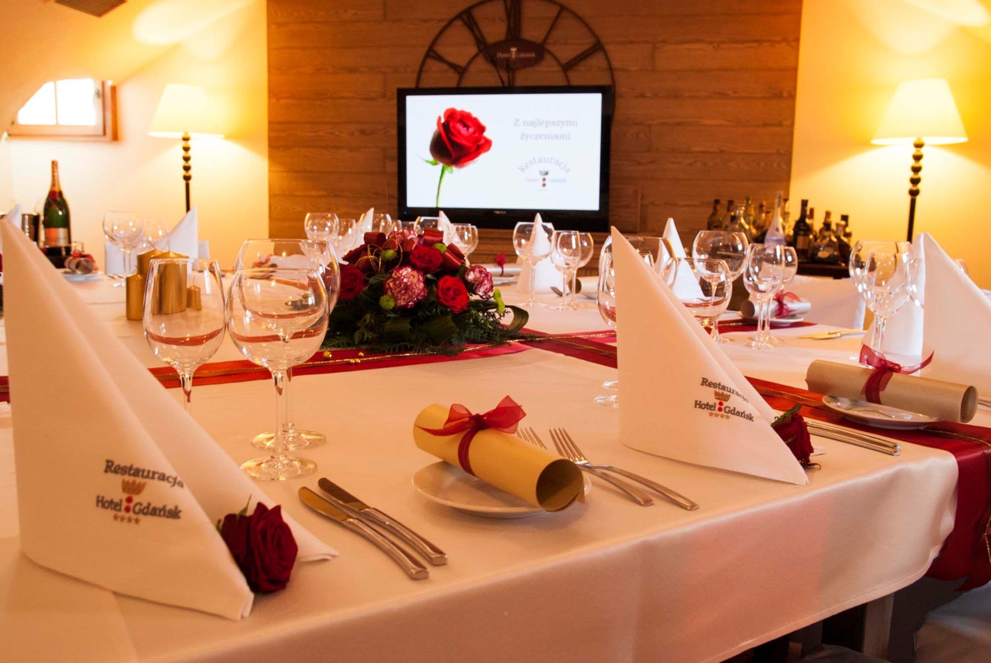 Una mesa de comedor dispuesta para un evento formal, con copas de vino, platos y un ramillete de rosas rojas.