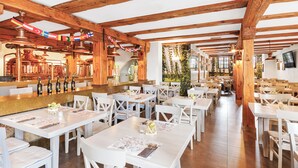 Un restaurante con vigas de madera, mesas blancas y una zona de bar con botellas.