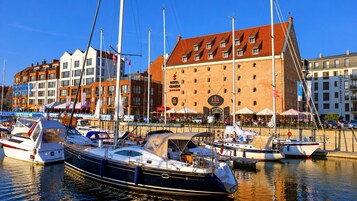 A marina with boats docked, a hotel building with a red roof, and a clear blue sky.