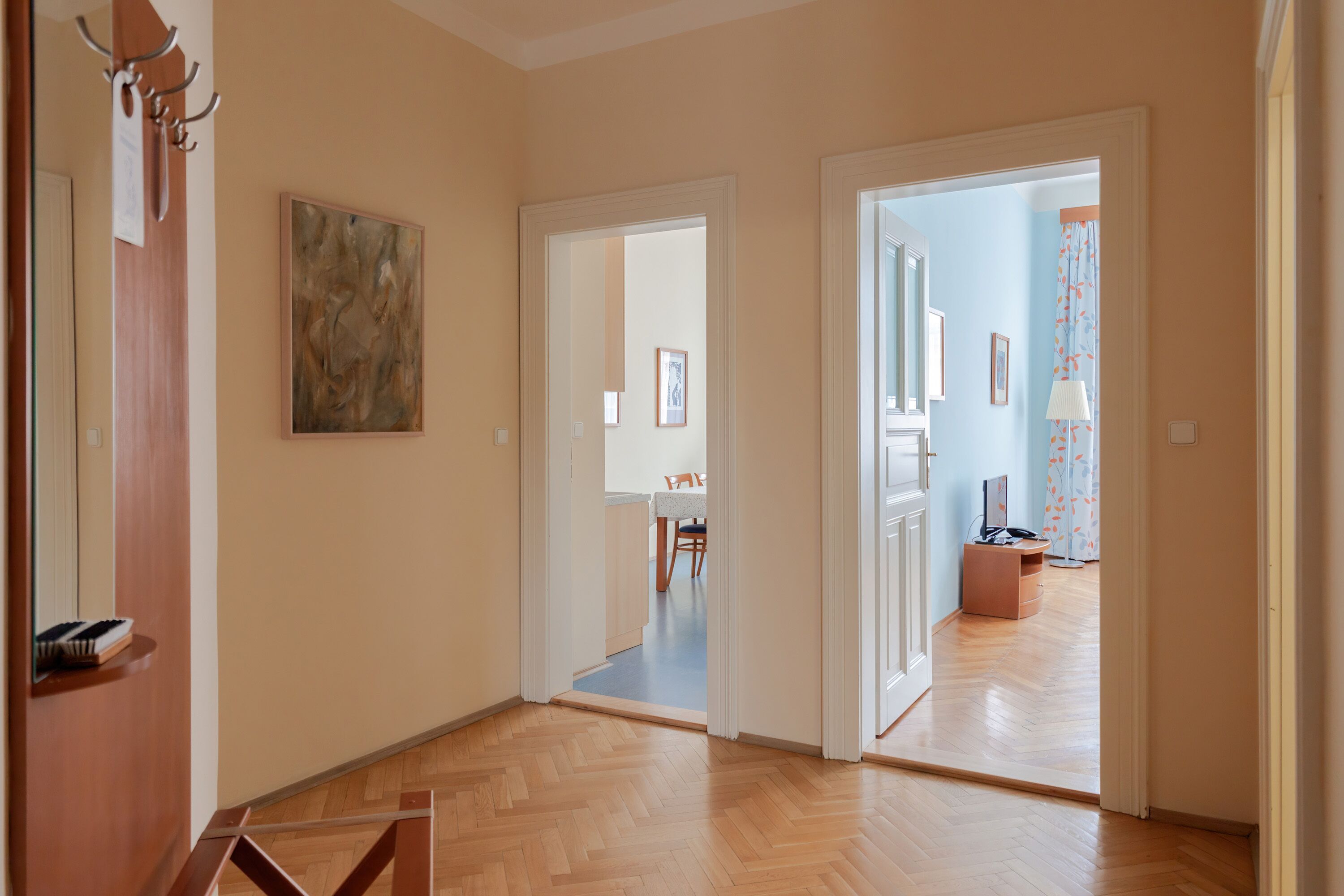 Un couloir doté d’un plancher en bois, un tableau accroché au mur et une porte donnant sur une autre pièce.