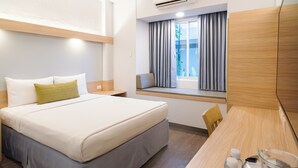 Habitación de hotel con cama, escritorio, silla, ventana con cortinas y un equipo de aire acondicionado.