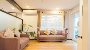 Una habitación con dos sofás, una planta, un extintor y una ventana con persianas.