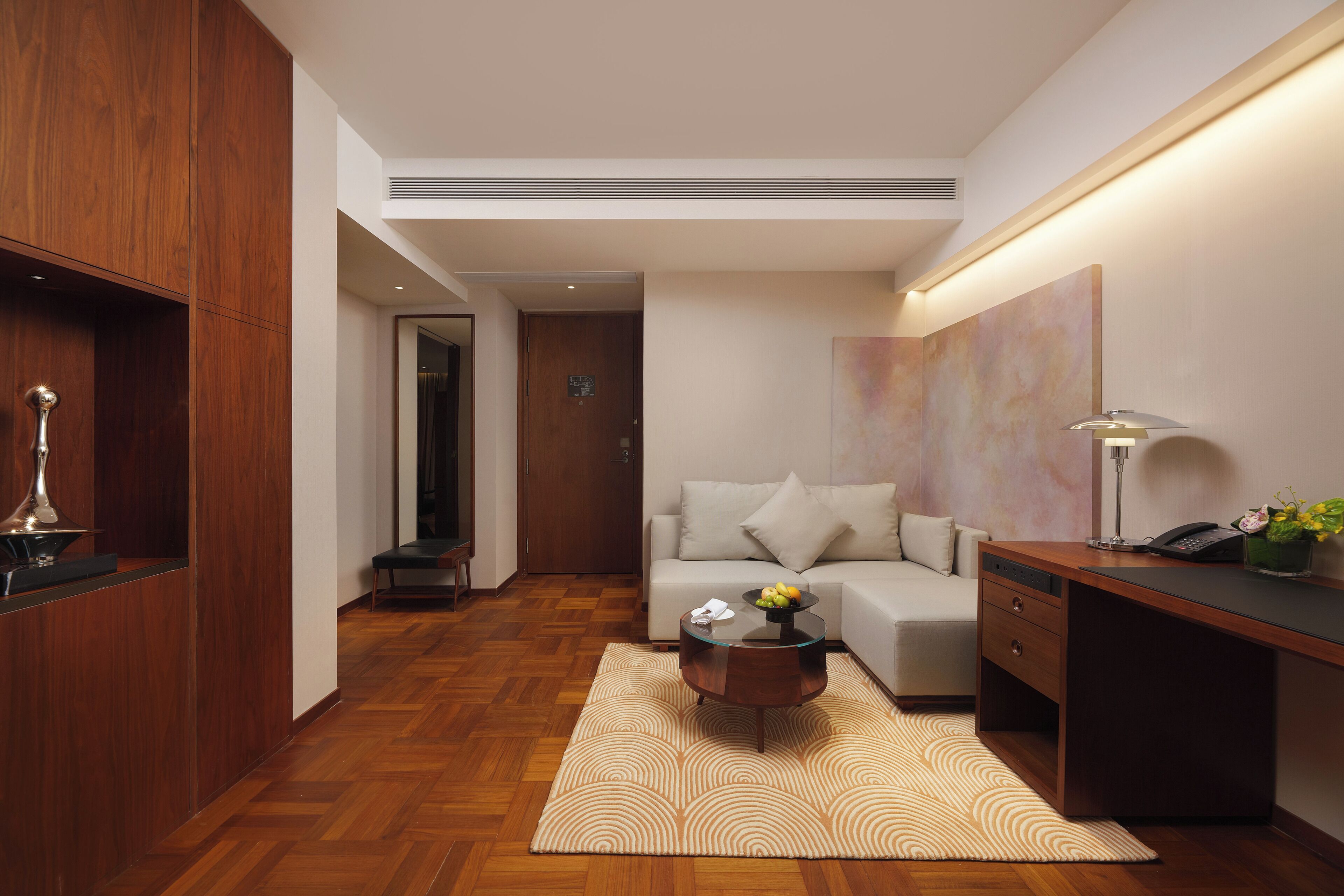 A modern hotel room with a wooden desk, a glass coffee table, a sofa, and a large abstract painting on the wall.