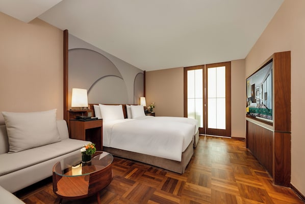 Una habitación de hotel con cama, sofá, mesa de centro de vidrio y televisor.
