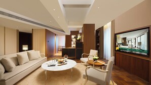 A modern hotel room with a sofa, a round coffee table, a TV, and a kitchen area.