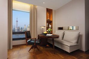 Une chambre d’hôtel avec vue sur les toits de la ville, un canapé, un fauteuil, une petite table avec une lampe et une étagère décorative.