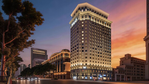 A high-rise hotel with a prominent 'Maxx' sign, surrounded by other buildings and a tree-lined street.