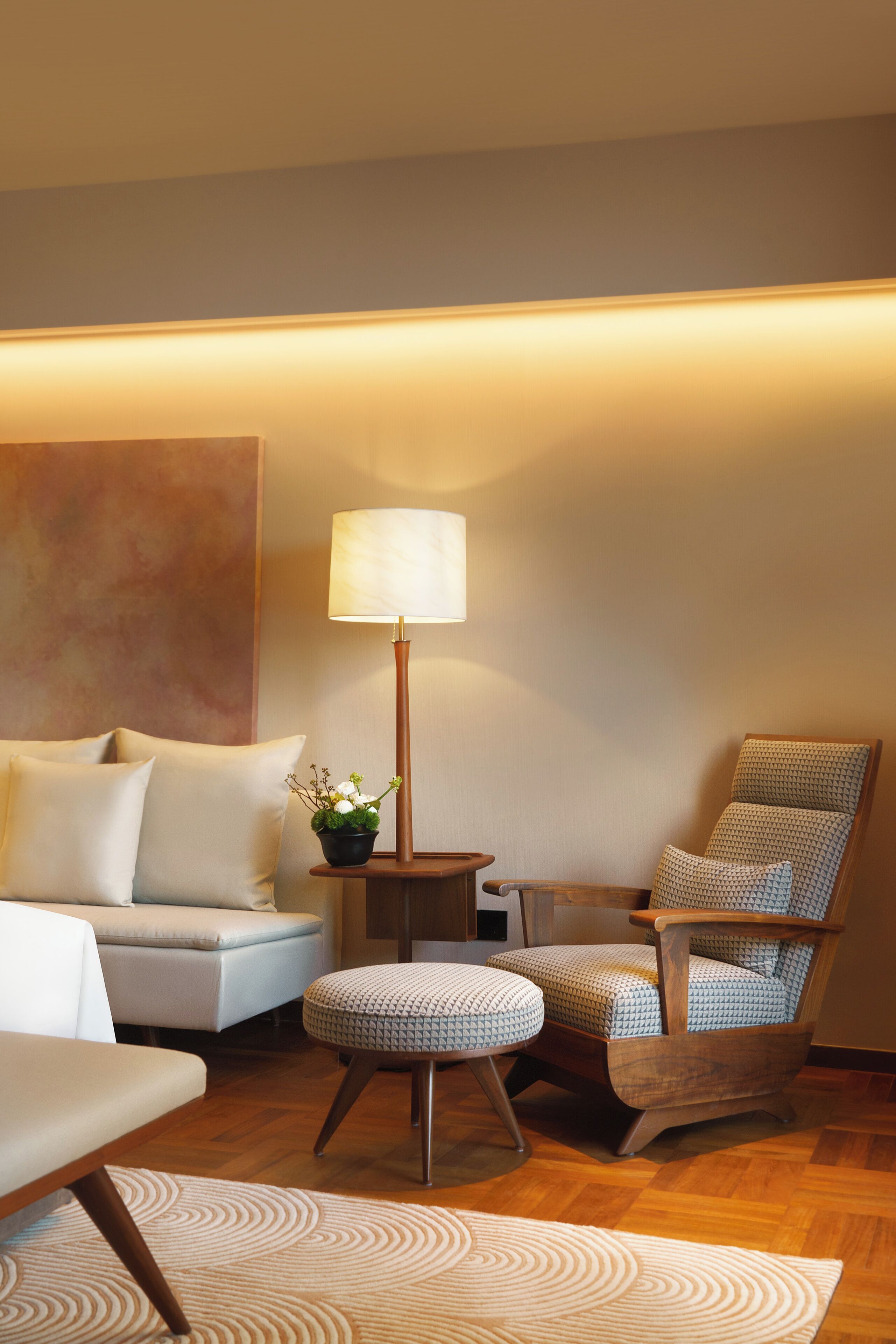 A modern living room with a sofa, ottoman, wooden chair, floor lamp, and a small table with a plant.