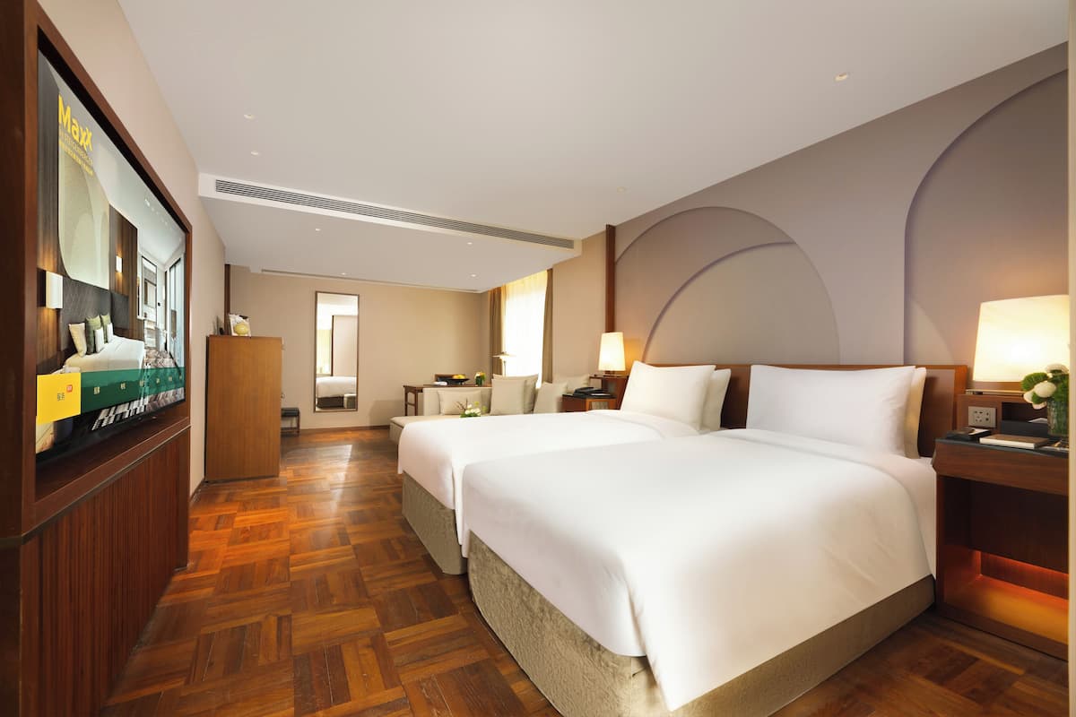 A hotel room with two beds, a television, a desk, and a large window.