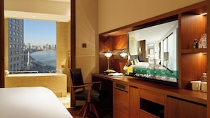 A hotel room with a large bed, a desk with a computer, a chair, a television, and a view of a cityscape.