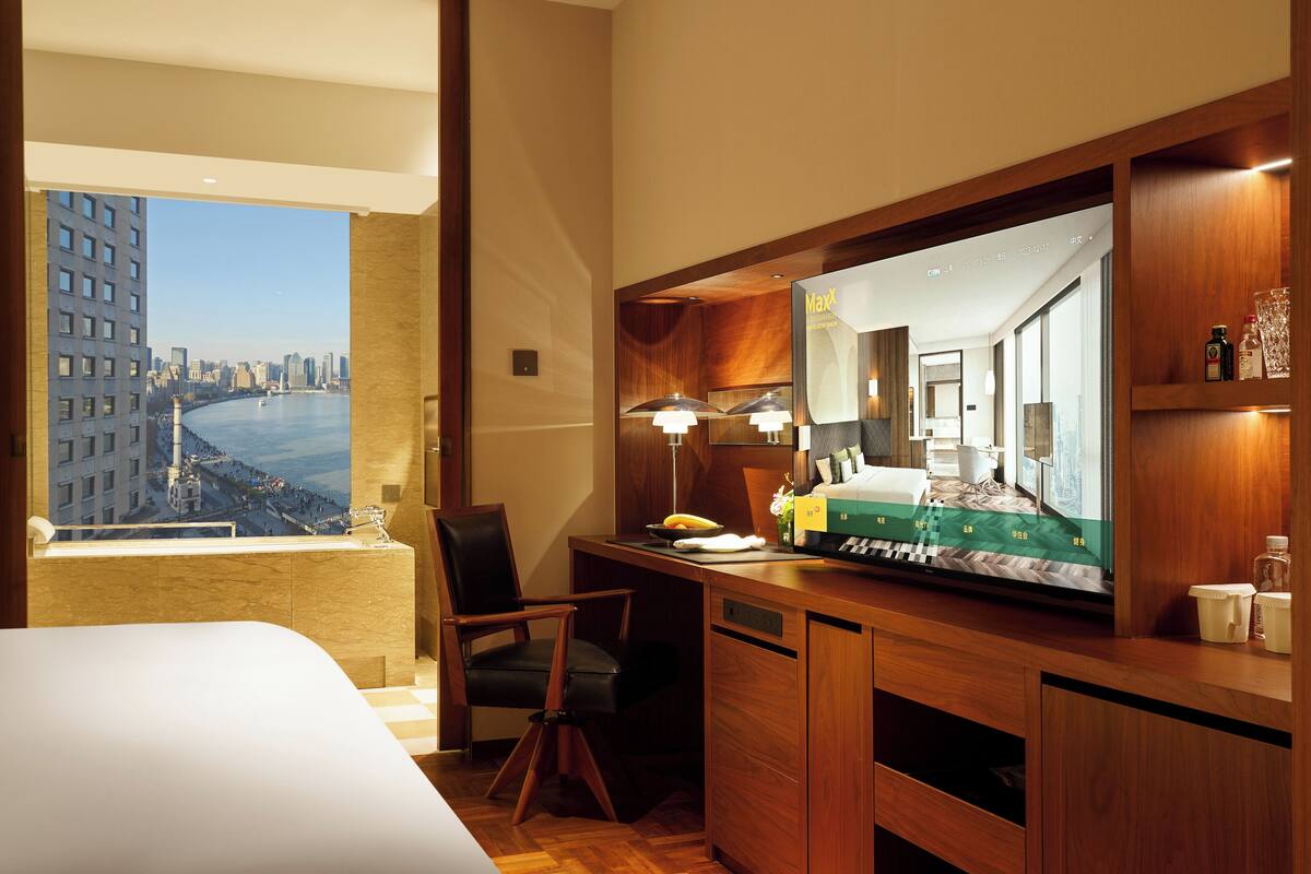 A hotel room with a large bed, a desk with a computer, a chair, a television, and a view of a cityscape.