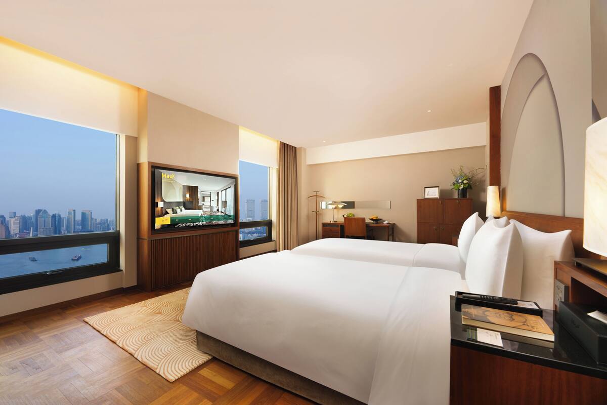 A hotel room with a large bed, a desk, a TV, and a view of a cityscape.