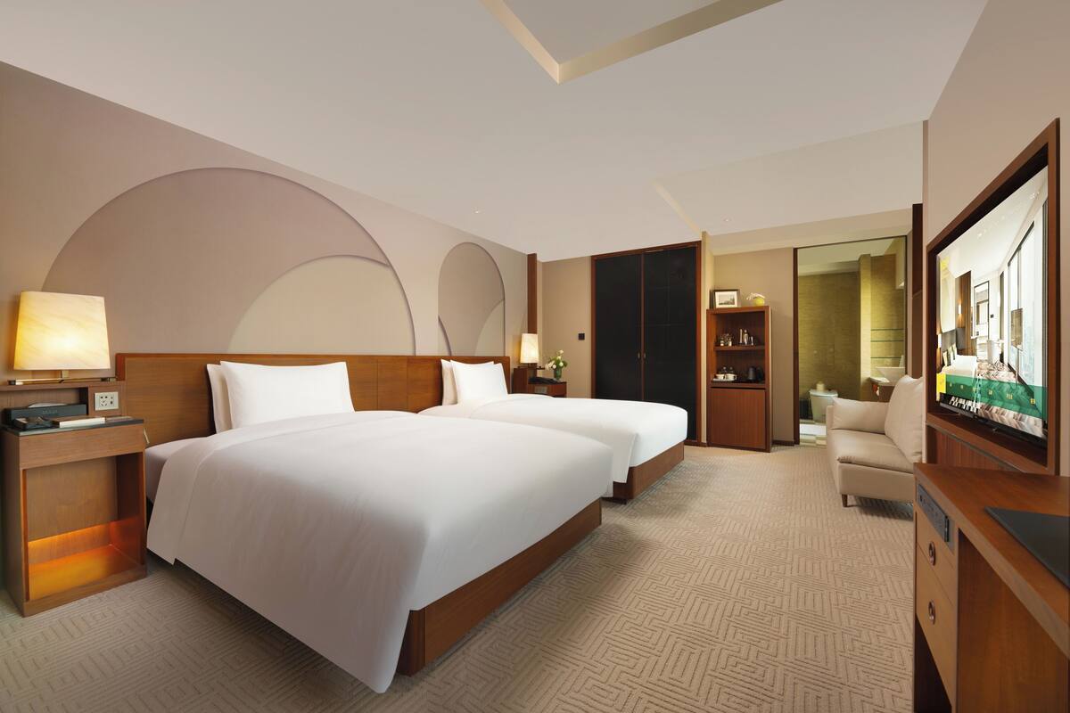 A hotel room with two beds, a flat-screen TV, a desk, and a sofa.