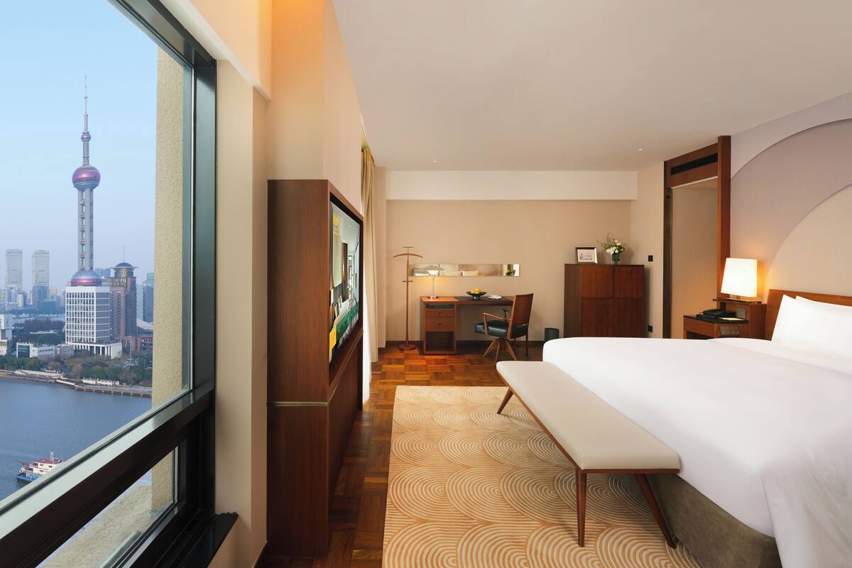 A hotel room with a large window, a bed, a desk, and a chair.
