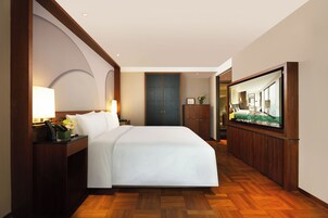 A hotel room with a bed, bedside lamps, a television, a wooden floor, and a wardrobe.