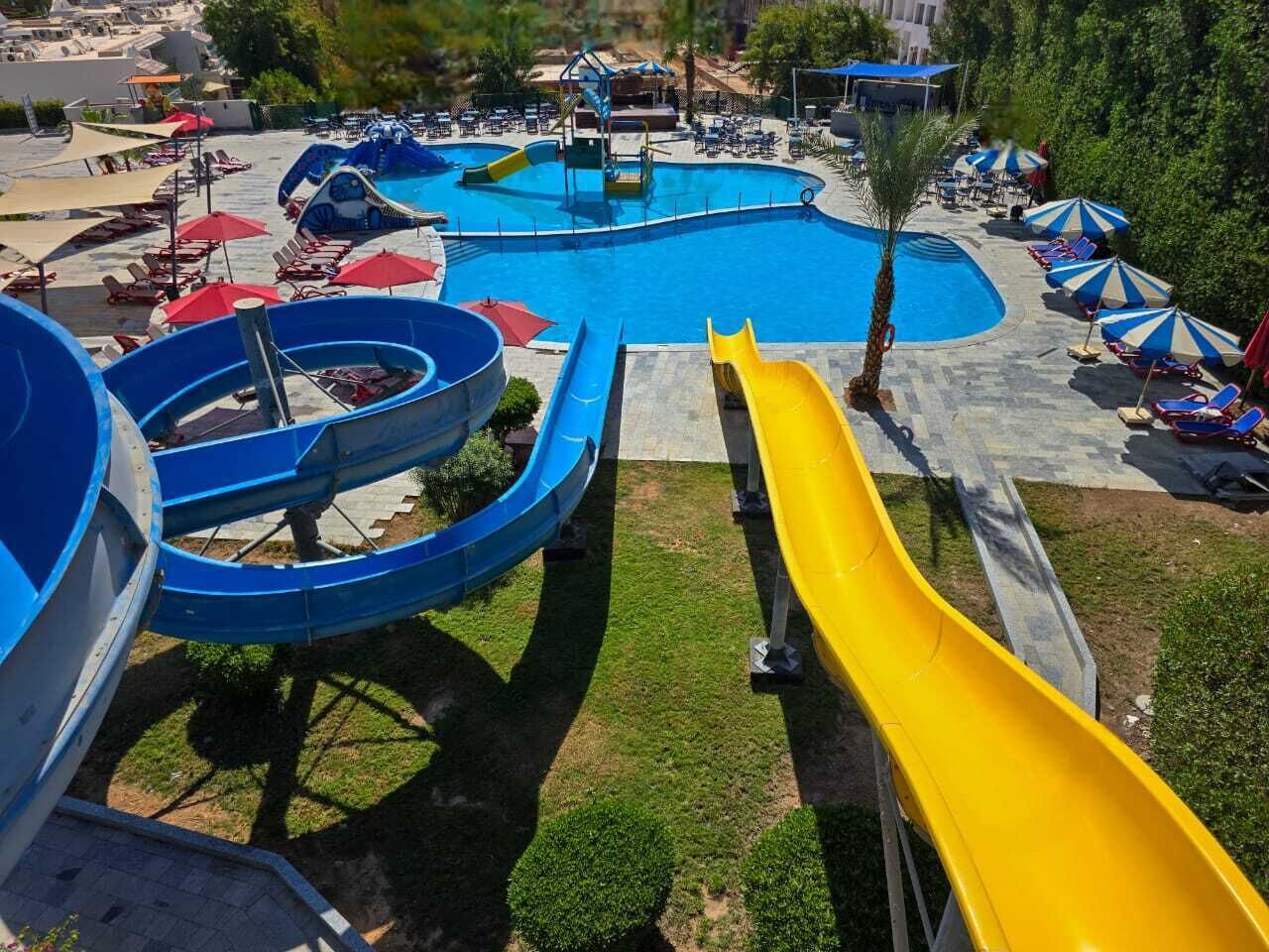 Una grande piscina all'aperto con due scivoli, circondata da lettini e ombrelloni.