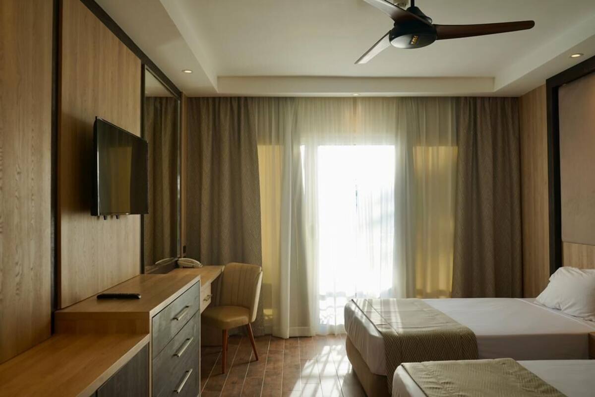 Une chambre d’hôtel équipée d’un lit, d’un bureau avec une chaise, d’une télévision et d’un ventilateur de plafond.