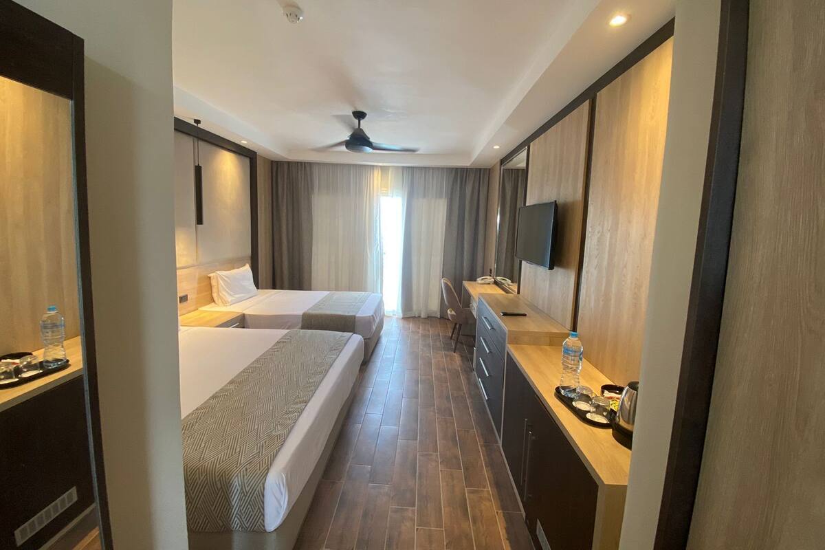 Une chambre d’hôtel avec deux lits, un bureau, une chaise, une télévision et un ventilateur de plafond.