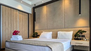 A modern hotel room with a large bed, a wooden headboard, a bedside table with a plant, and a nightstand.