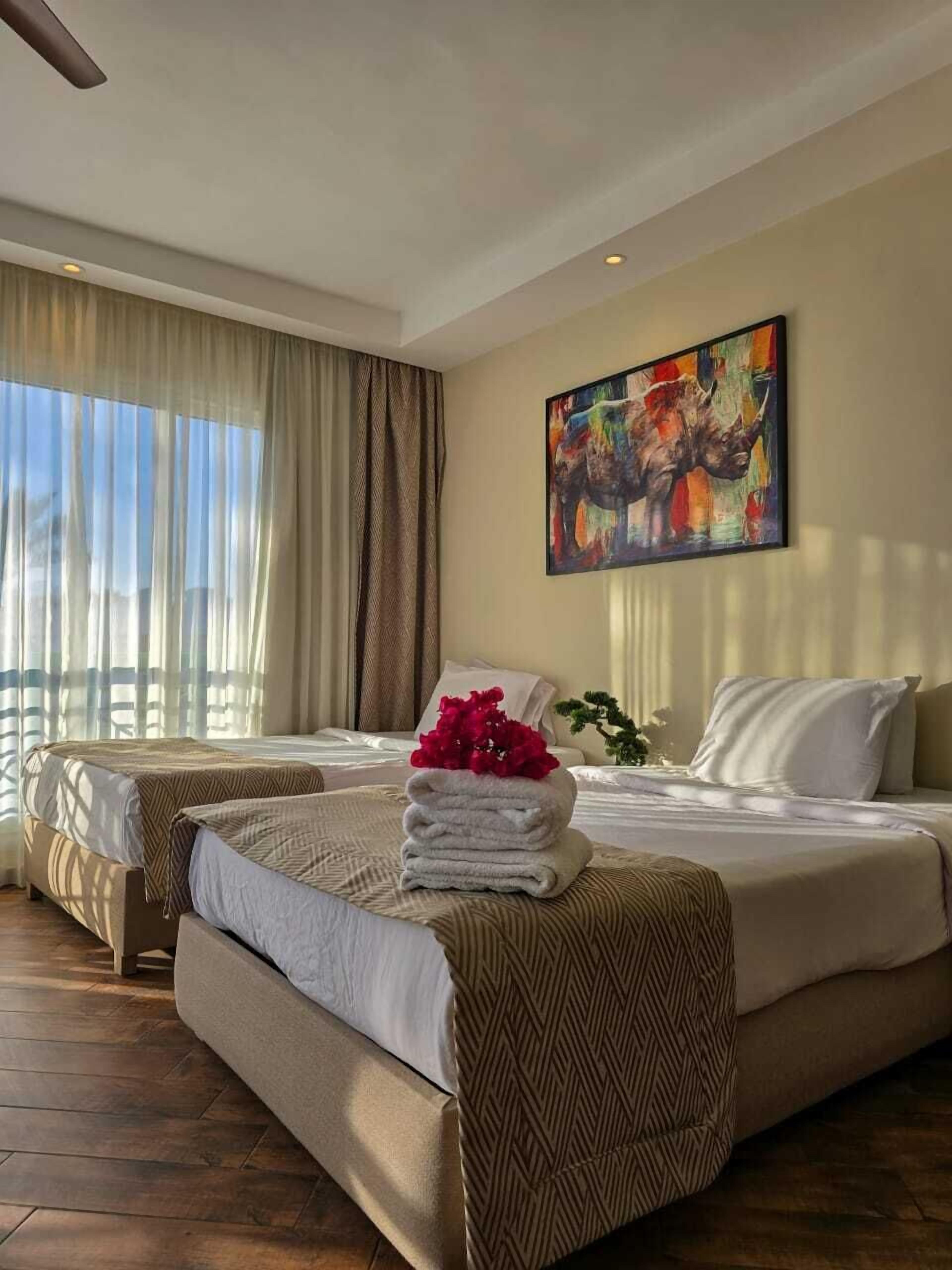 A hotel room with a bed, a desk, a painting, and a window with curtains.