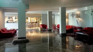 A spacious lobby with a polished marble floor, red seating, and a view of a restaurant area.