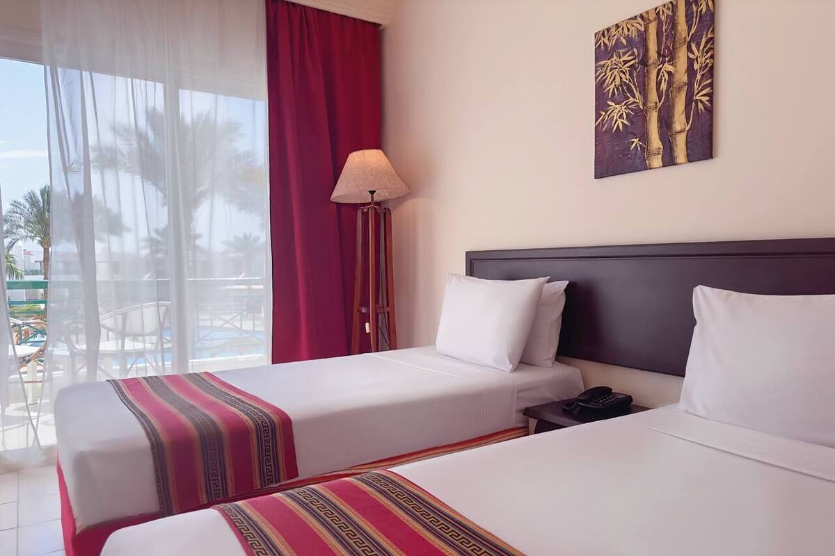 Une chambre d’hôtel avec deux lits, une table de chevet, une lampe et un tableau au mur.