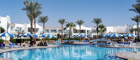 A pool area with blue and white striped umbrellas, lounge chairs, and palm trees.