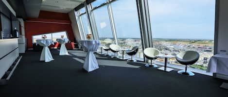 Una sala de conferencias moderna con ventanas amplias, mesas blancas y sillas dispuestas para reuniones.