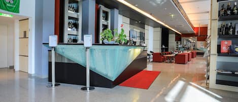 A modern hotel lobby with a reception desk, seating area, and a bar.