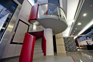 Un interior moderno con una escalera en espiral, barandilla de vidrio y un papel tapiz estampado.