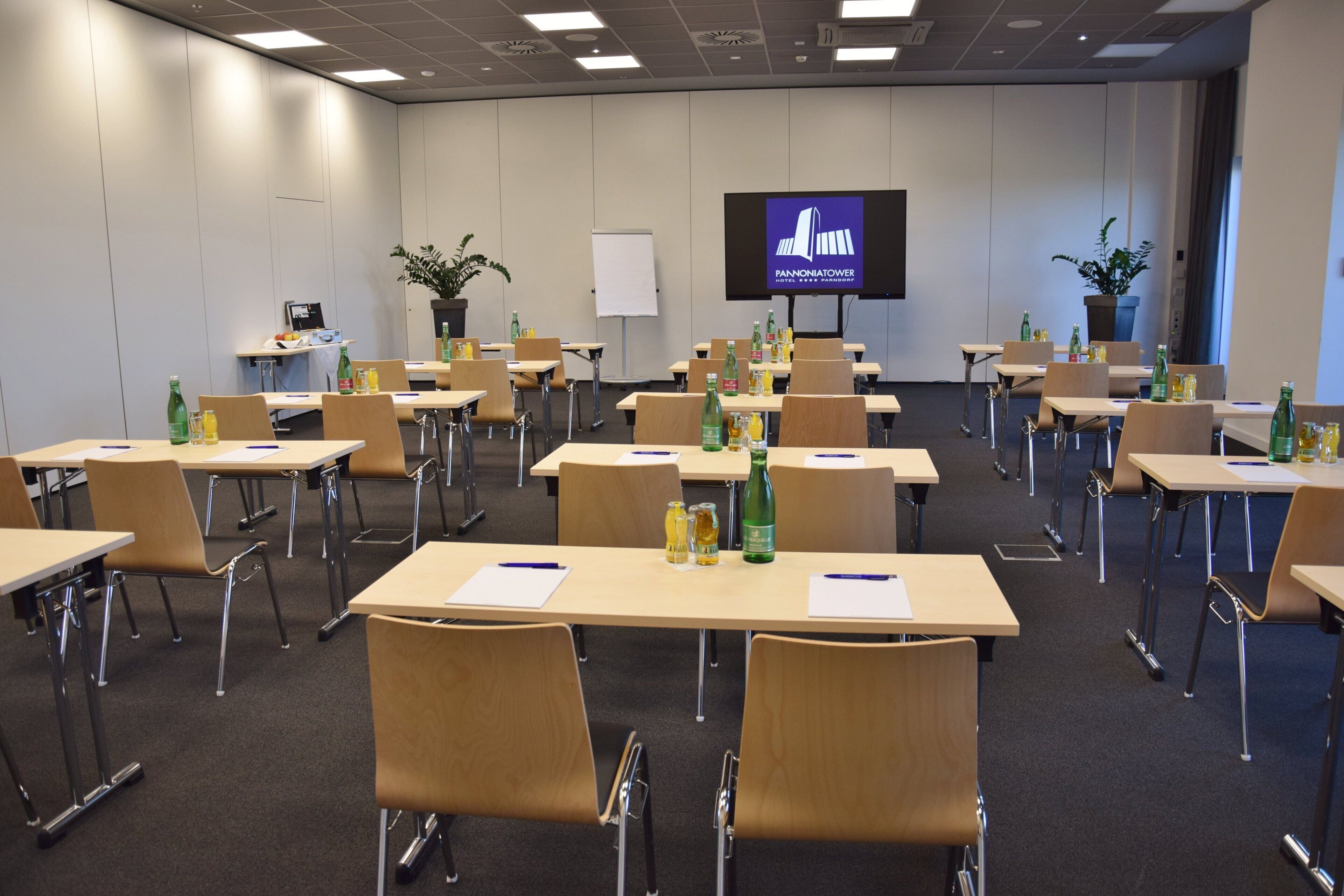 A conference room with multiple tables and chairs, a whiteboard, a television screen, and potted plants.