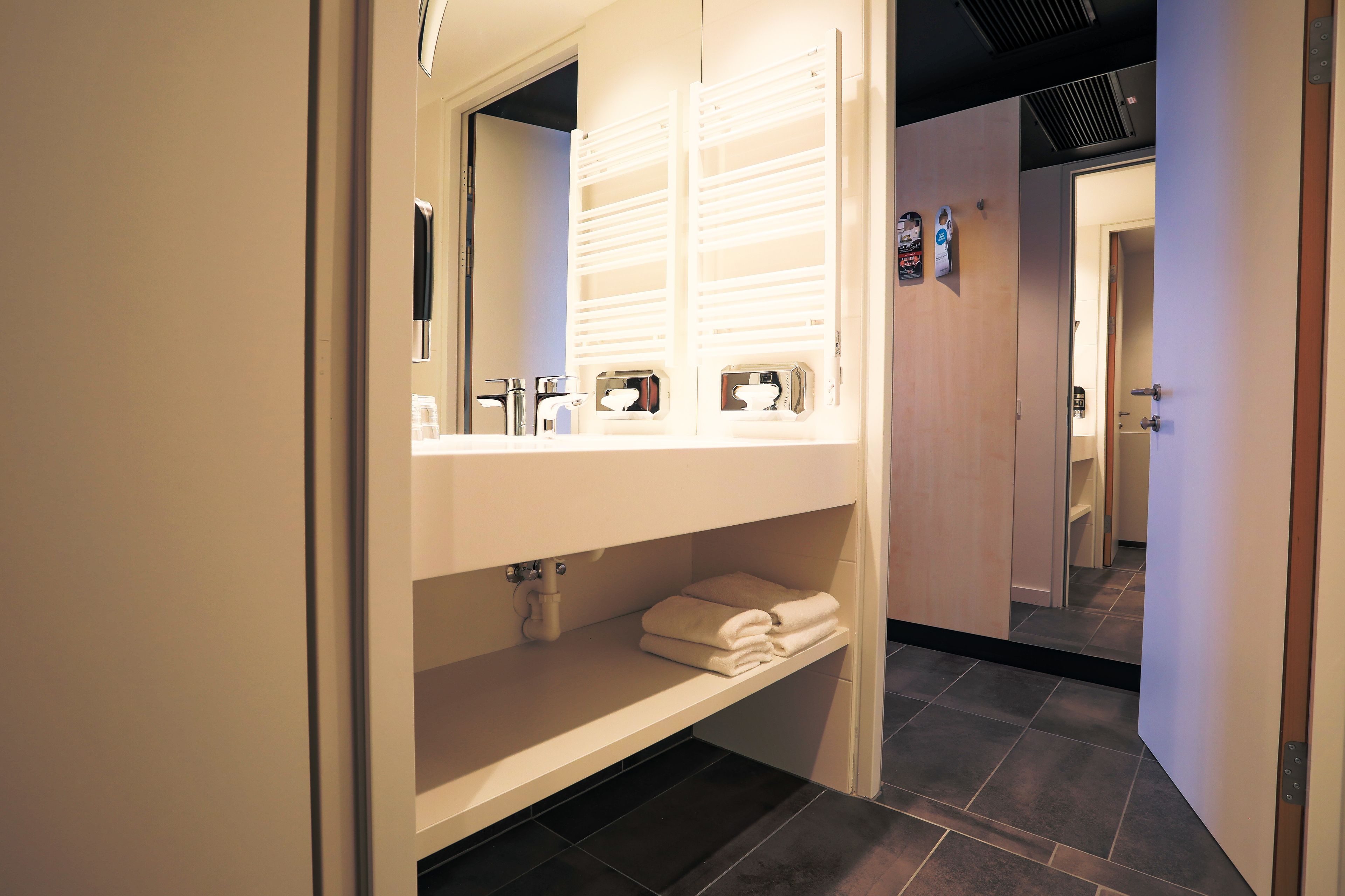 Une salle de bain moderne dotée d’un grand miroir, de porte-serviettes intégrés et d’une étagère pour les articles de toilette.