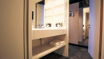 A modern bathroom with a large mirror, built-in towel racks, and a shelf for toiletries.