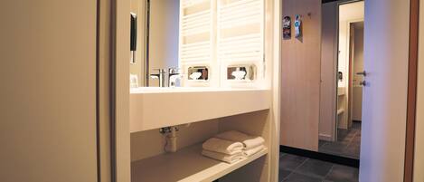 Un baño moderno con un espejo grande, toalleros empotrados y un estante para artículos de aseo.