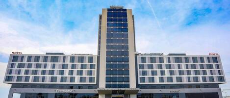 A modern hotel with a central tower, a restaurant, and a parking garage.