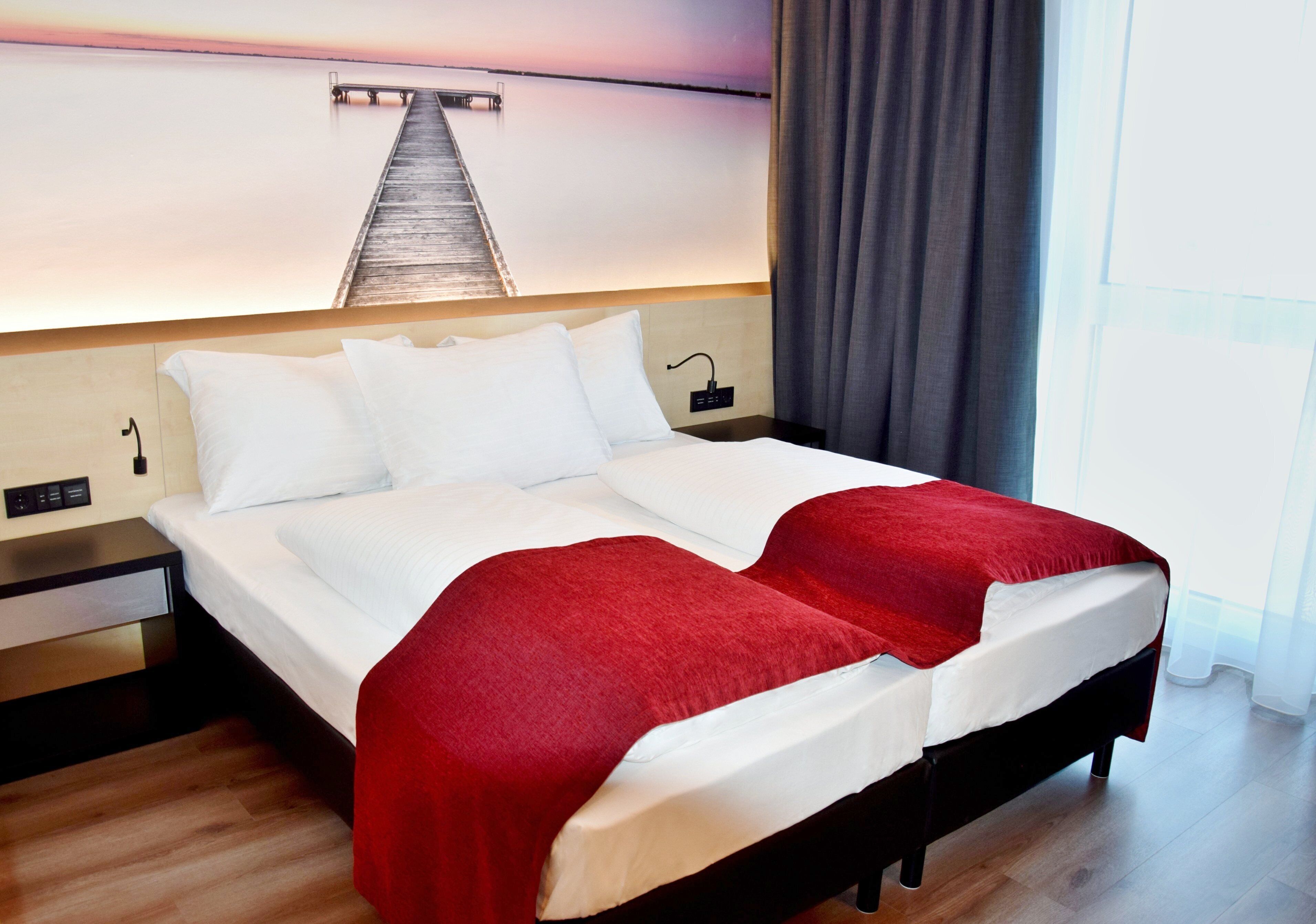 A hotel room with a large bed, a wooden headboard, a nightstand, and a view of a pier.