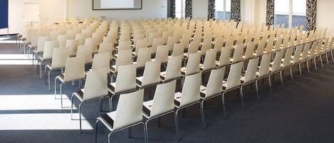 Une salle de conférence avec des rangées de chaises, un écran de projection et un tableau blanc.