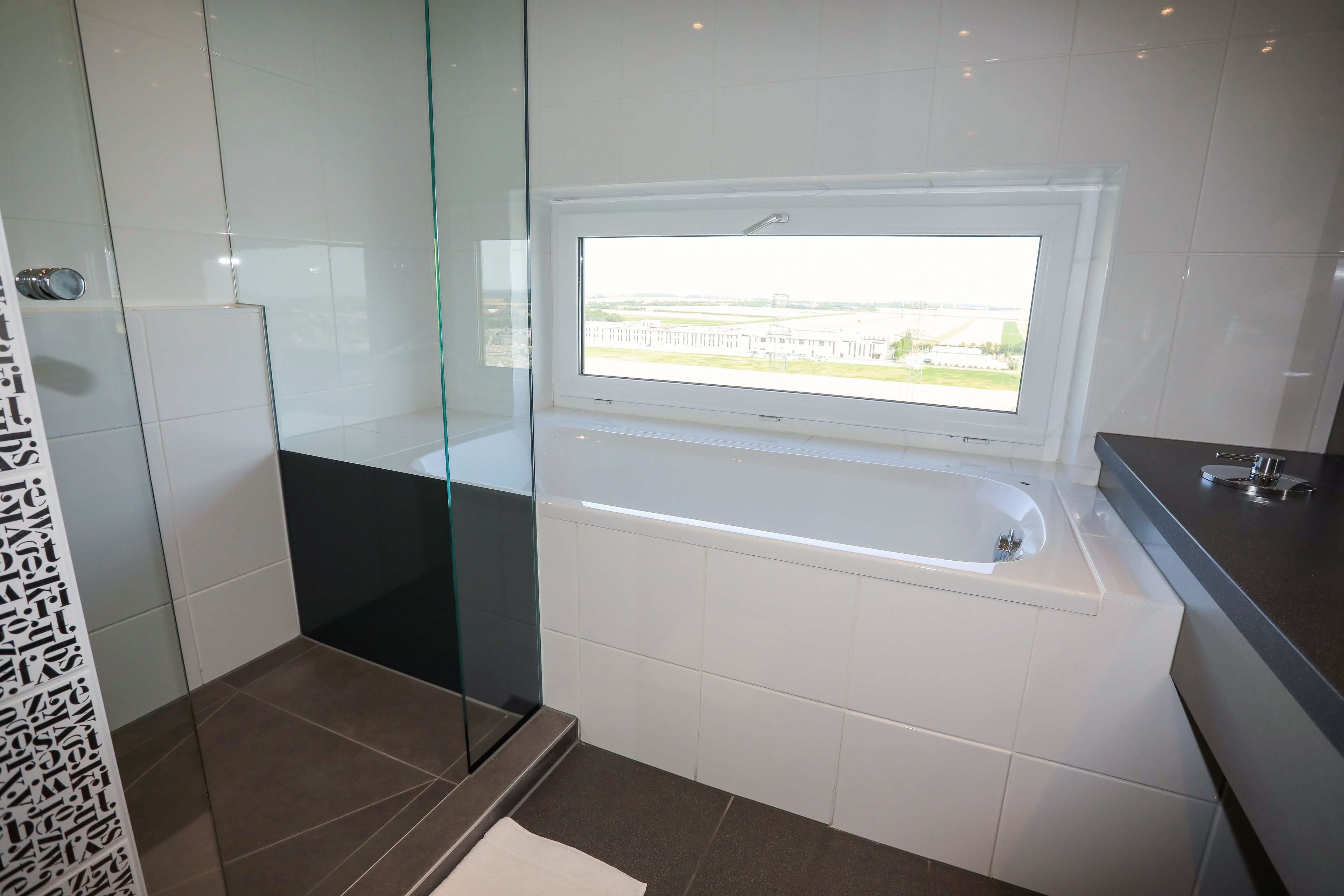 A modern bathroom with a glass shower enclosure, a bathtub, and a window providing a view of the outdoors.