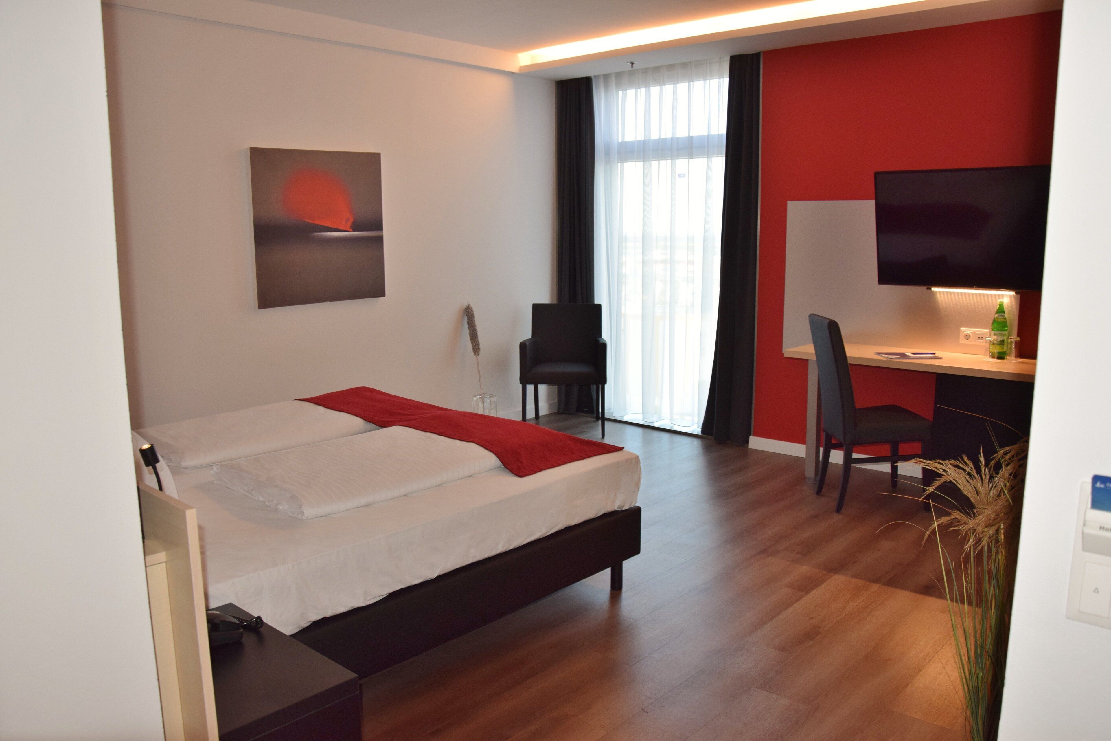 A hotel room with a bed, a desk, a chair, a TV, and a window with curtains.