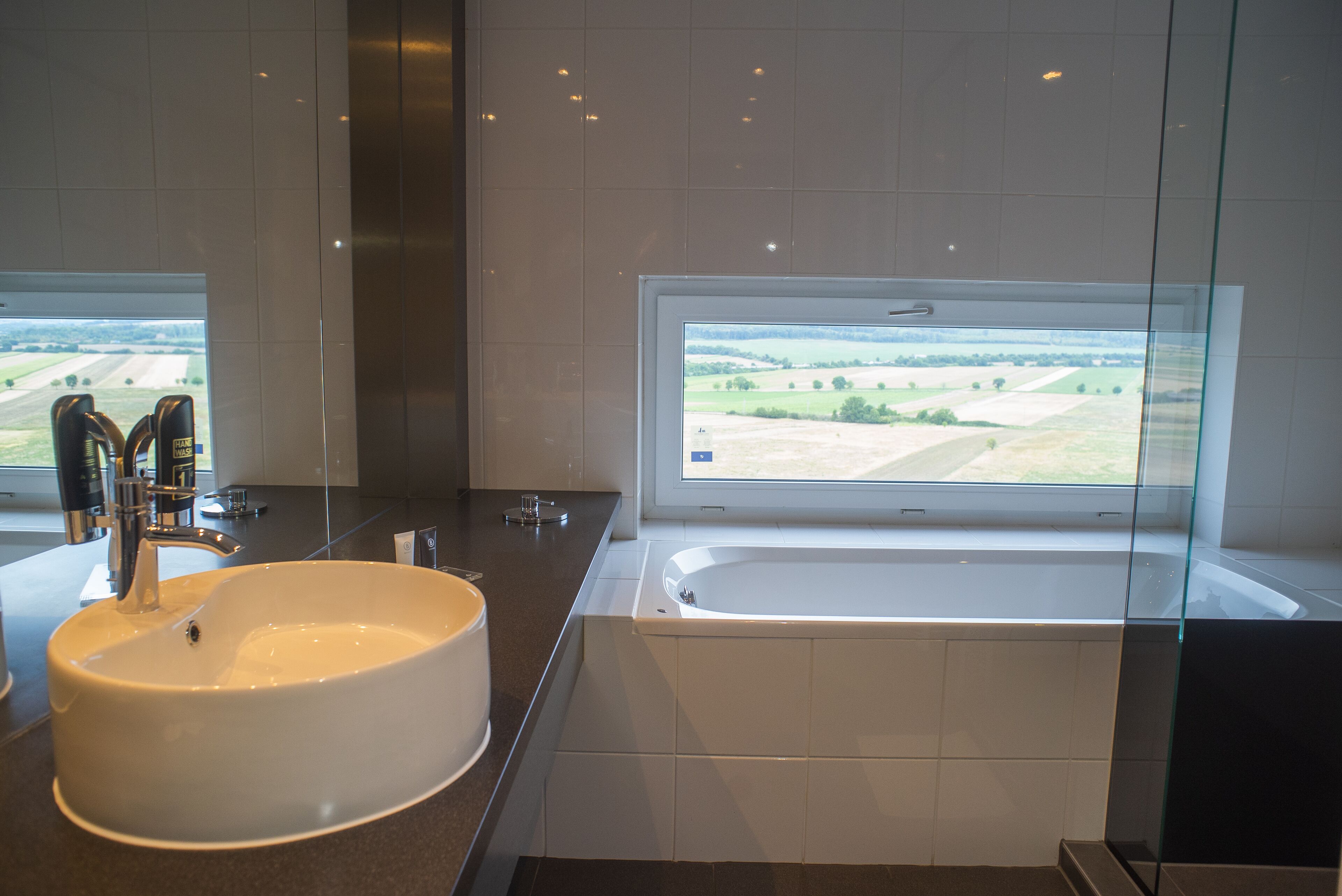 A bathroom with a large sink, a bathtub, and a window offering a view of fields.