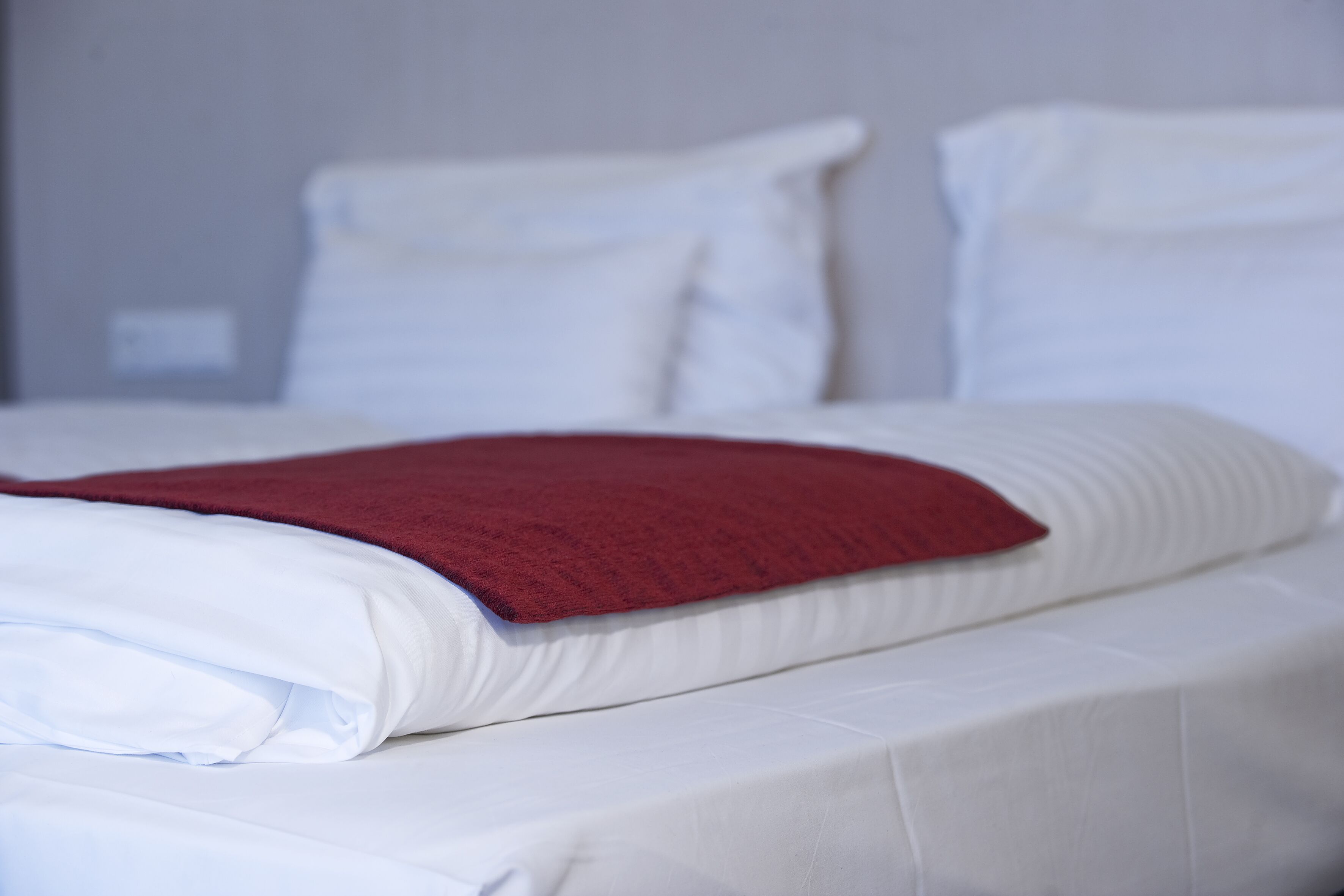 A neatly made bed with white linens and a red blanket.