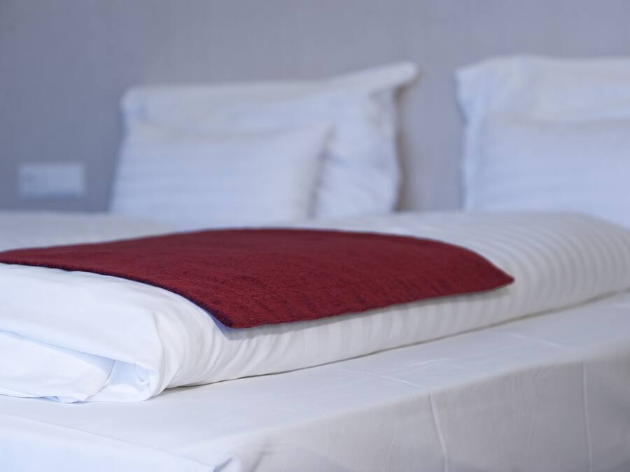 Un letto rifatto con lenzuola bianche e una coperta rossa.