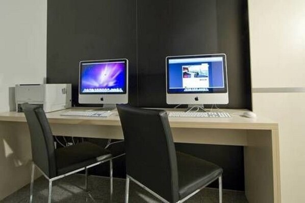 Two Apple iMac computers on a desk with two black chairs. - Pannonia Tower Hotel Parndorf (Parndorf)