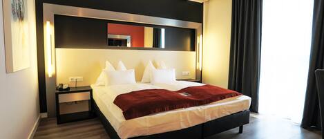 Una habitación de hotel moderna con una cama grande, una mesita de noche con un teléfono y una lámpara.