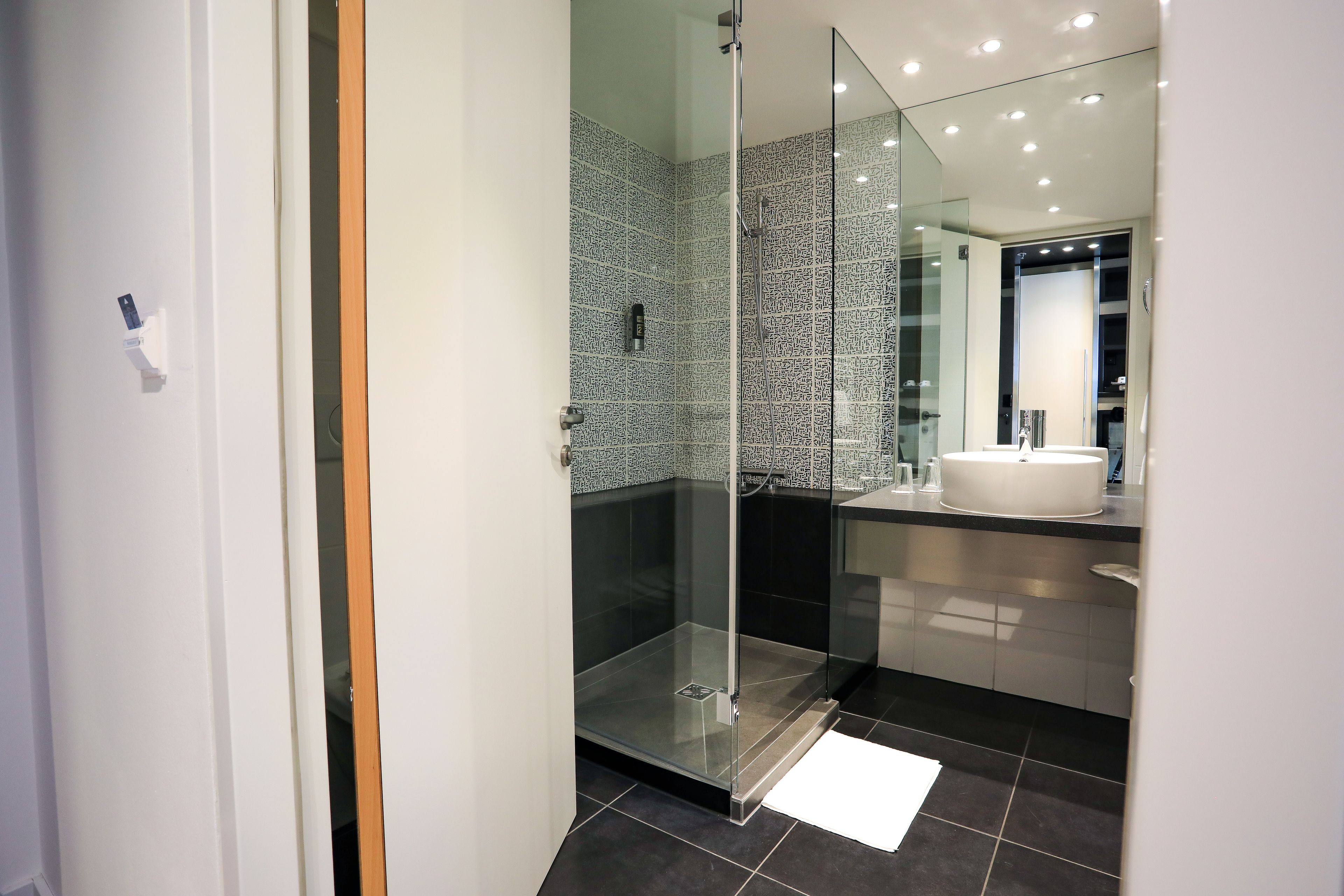A modern bathroom with a glass-enclosed shower, a white sink, and a tiled floor.
