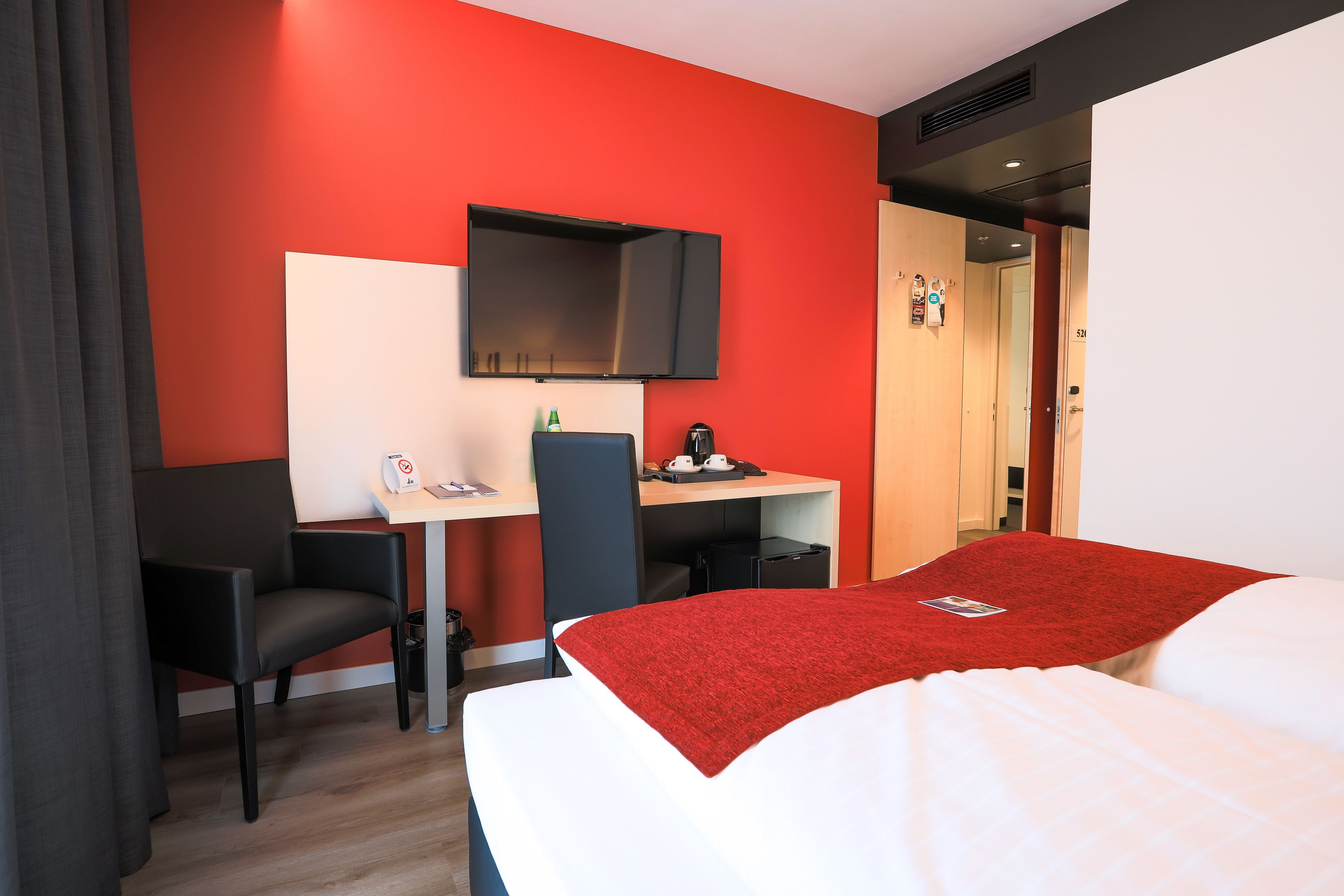 A hotel room with a bed, a desk, a chair, a TV, and a door.